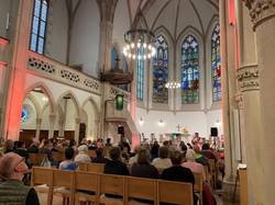 Quelle: Pfarrerin Mirjam Keim Innenraum der bunt beleuchteten Evangelischen Stadtkirche in Baden-Baden während des Aperol-Gottesdienstes am 13. September 2025. Die Besucher sitzen auf Holzbänken und blicken zum Altar, wo die junge Band der Petrusgemeinde Rastatt spielt.